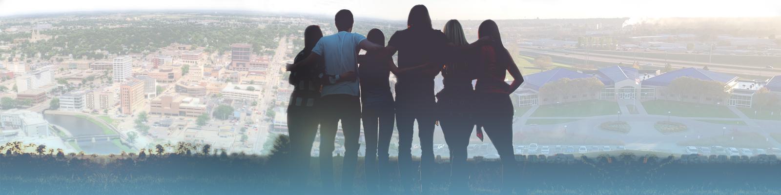 silhouettes of a group of people with Sioux Falls and Southeast Tech in background